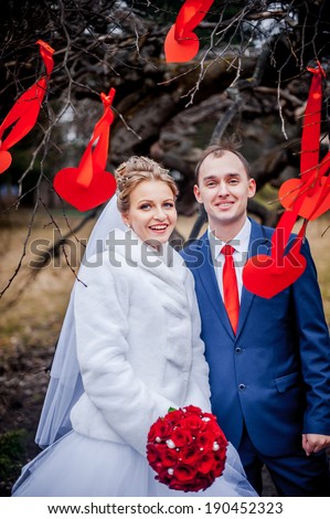 young wedding couple, beautiful bride with groom portrait on outdoor. tree decorated with red hearts. Funny couple
