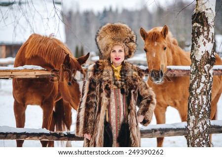 Winter beautiful Girl in  Fur Coat and hat feed the horses