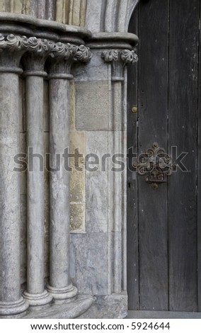 Stone columns next to a wooden door with an ornamental door handle or knocker
