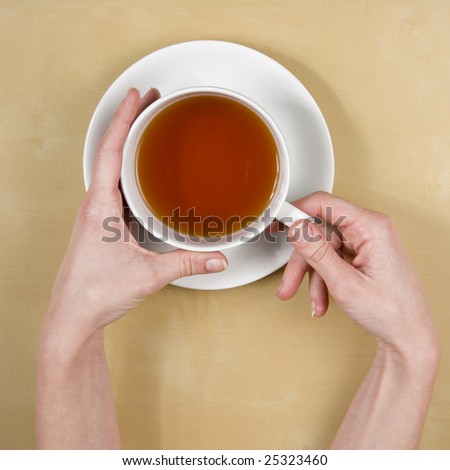 tea - top view of female hands holding a cup of tea on a light wood table