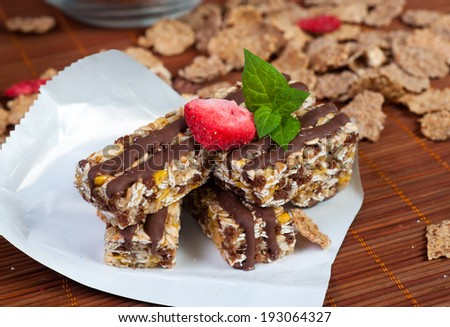 bar of chocolate muesli with petals poured with raisins with chocolate in the background milk in the dark key