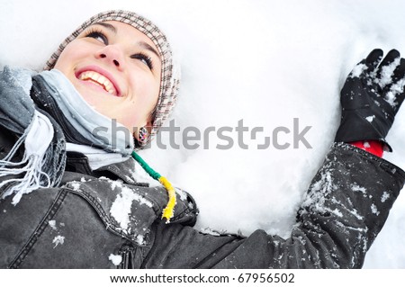 Young brunette woman with winter outfit lying on snow making snow angel.