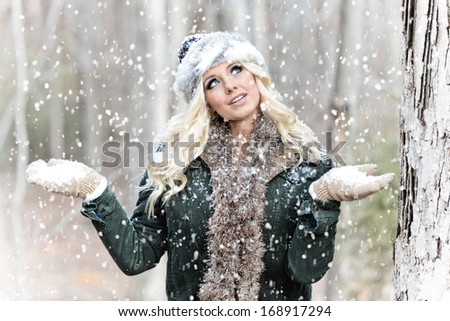 Pretty young woman in the snow wearing a coat, scarf, hat and mittens outdoors