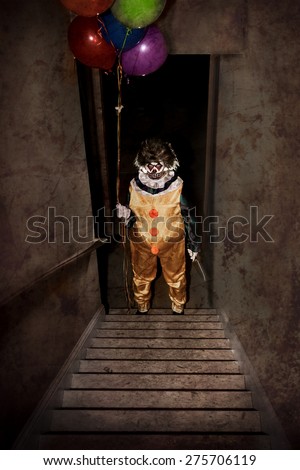 Scary Clown standing at the bottom of a stairway holding balloons and a knife