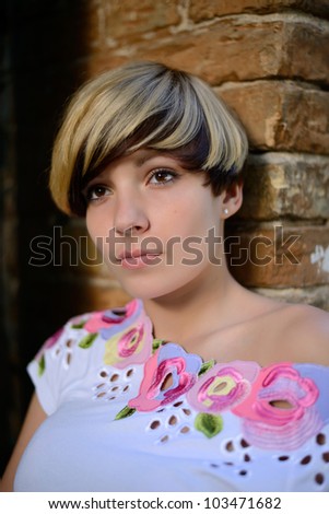 Beautiful girl with modern haircut standing near a brick wall