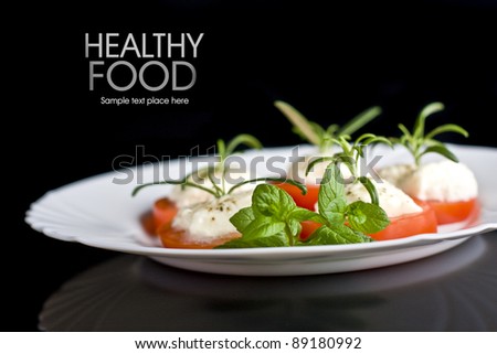 Tomatoes with mozzarella and rosemary on white plate isolated on black background