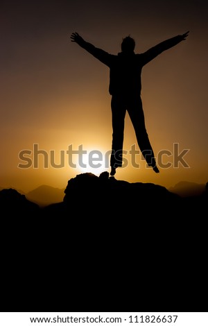 A silhouetted person jumping in front of the rising desert sun