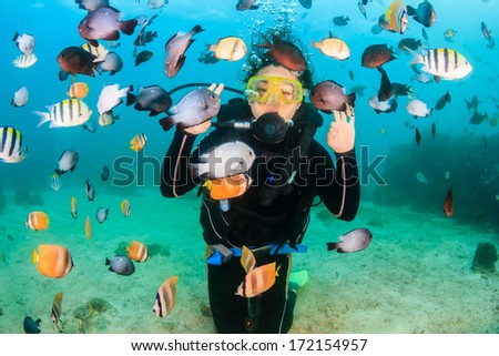 Smiling female SCUBA diver surrounded by colorful tropical fish