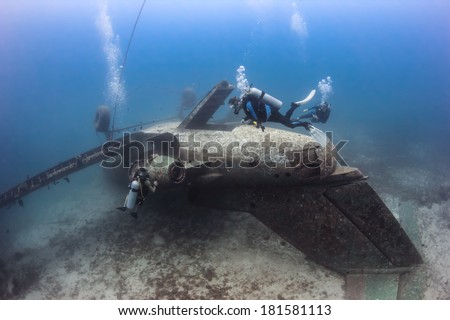 SCUBA divers exploring the upturned fuselage of an underwater aircraft wreck
