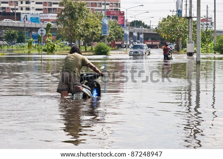 PATHUMTHANI, THAILAND - OCTOBER 18 -Thai flood hits Central of Thailand, man leading his motorcycle navigating through the flood- Tuesday october 18, 2011 in Pathumthani, Thailand
