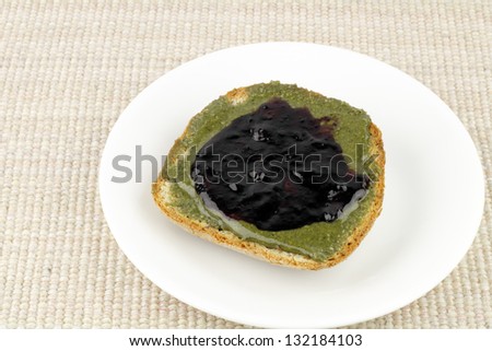 Smooth green hemp butter with blueberry fruit preserves spread on whole grain bread is a deliciously healthy snack full of balanced Omega fatty acids 3, 6, and 9.