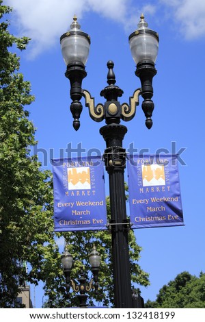 PORTLAND, OREGON - JULY 28: Two Portland Saturday Sunday Market signs hung below street lights with trees and a beautiful sunny blue sky in the background on July 28, 2012 in Portland, Oregon.