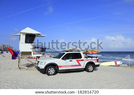 POMPANO BEACH, FLORIDA - DECEMBER 22, 2013: Pompano Beach Ocean Rescue truck next to a lifeguard tower with rescue surfboards, safety warning flags, with people and the Atlantic ocean on a sunny day.