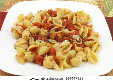 Small conchigliette pasta shells prepared with diced tomatoes, many peeled garlic cloves, parsley, basil and oregano served on a white plate with a colorful background.