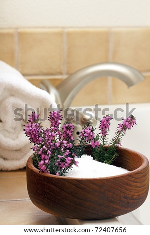 Pretty heather flowers in a bowl of Epsom salts on a bath tub edge ready to bathe.