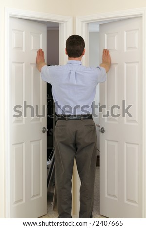 Man in the middle of two doors pushes open both at the same time and needs to choose which to walk through.