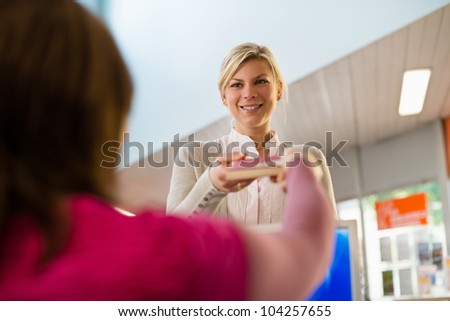 Portrait of young female college student returning book to librarian in public library