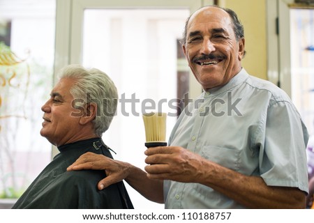 Old barber holding brush for talco and smiling to camera in old fashion barber shop