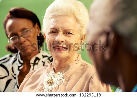 Active retired elderly women and free time, group of happy senior african american and caucasian female friends talking and sitting on bench in park