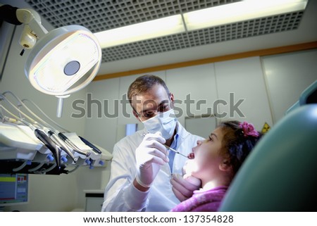 Doctor during visit of female child in dental clinic, dentist checking teeth of young baby girl