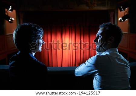 Arts and entertainment in theatre, with man and woman looking at stage with red curtains