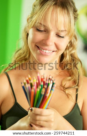 Portrait of young woman holding bunch of colorful pencils at camera and smiling