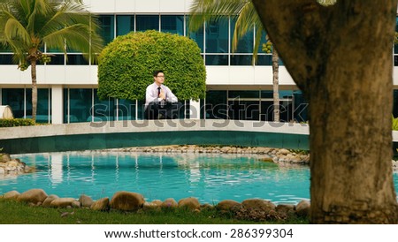 Asian businessman relaxing outside office building. The man does yoga on a bridge and smiles with eyes closed in prayer position