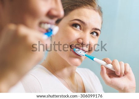 Young couple living together, washing teeth in bathroom in the morning. The woman looks happily at her boyfriend. Concept of new relationship and beginnings