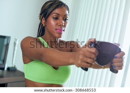 Young adult african american woman in sports clothing measuring body fat with electronic tool. The girl holds the sensors with her hands and looks at the display