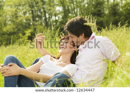 Couple lying in grass, man tickling her girlfriend\'s nose and smiling