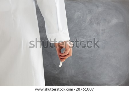 rear view of female teacher in lab clothes holding chalk against blank blackboard. Copy space