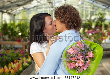mid adult couple kissing in flower nursery and holding bouquet