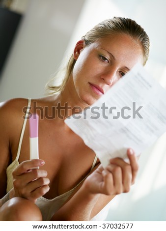blonde woman holding pregnancy test and reading information.