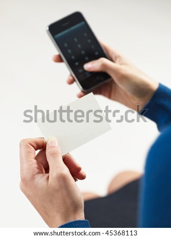 businesswoman holding blank business card and dialing numbers on mobile phone
