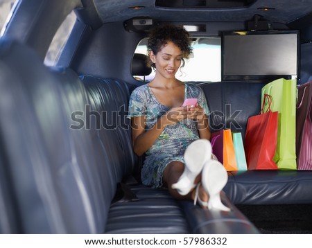 woman sitting in limousine with shopping bags and typing on mobile phone. Horizontal shape, full length, copy space