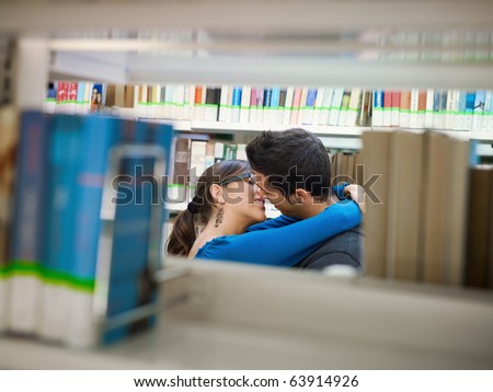 two caucasina students hugging and kissing behind shelves in library. Horizontal shape, side view, copy space