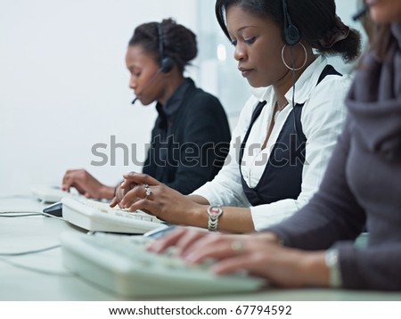 multiethnic group of female customer service representatives talking on the phone and typing on computer keyboard. Horizontal shape, side view, copy space