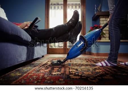caucasian heterosexual couple, with woman doing chores using vacuum cleaner on carpet and lazy man on sofa with tablet pc. Horizontal shape, low angle view