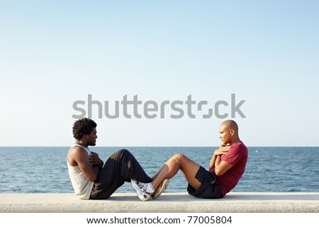 young african american man and hispanic friend doing series of sit-ups along the Caribbean sea in Havana, Cuba. Horizontal shape, full length, side view, copy space