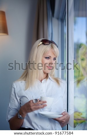 Mid adult businesswoman relaxing and drinking a cup of tea, looking out of window. Waist up, side view, copy space