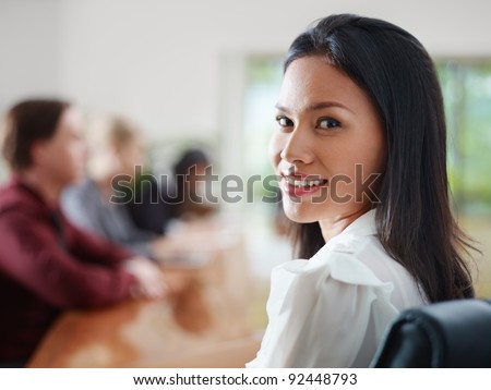 Attractive young Asian business woman smiling and looking over shoulders at business meeting with co-workers.