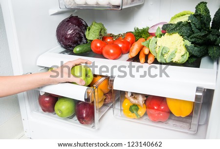 Hand Reaching for Green Apple in Refrigerator Full of Healthy Food Options