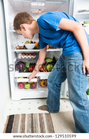 Boy Reaching for Apple in Refrigerator Full of Healthy Food Options