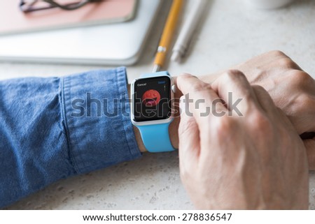 SEATTLE, USA - May 17, 2015: Man Wearing Sport Apple Watch with Blue Rubber Band. Red Faced Shocked Emoji Displayed.