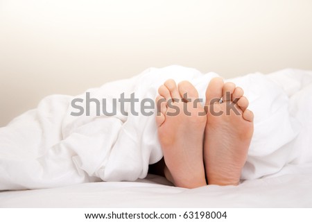 Pair of Feet in Bed on White Sheets