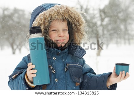 Funny small boy invites to drink hot tea from thermos at winter park