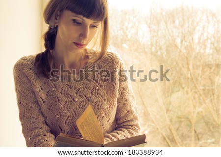 Young adult girl reading book near the window