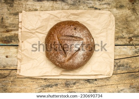 Whole loaf of bread with paper bag on old weathered wood background. Top view
