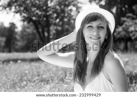 Young cheerful adult girl in summer park. Smiling woman with hat in outdoor environment. Black and white image