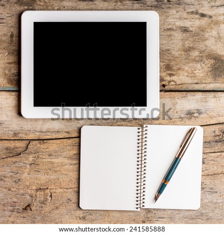 Digital pad with empty black screen and opened notebook with old fountain pen on wooden table